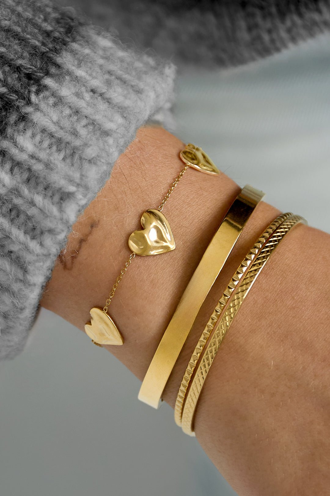 Gold bracelet with heart-shaped charms worn on the wrist along with other bracelets from Sorea Fashion.