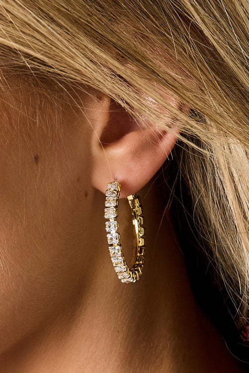 Gold hoop earrings with a smooth minimalist design worn in the ear, Rina earrings from Sorea Fashion.