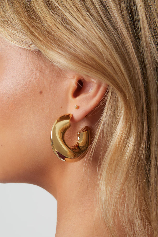 Gold Sol hoop earrings with a smooth round shape worn in the ear from Sorea Fashion.